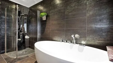 Moderne bad med mørke fliser, frittstående badekar og dusjhjørne.