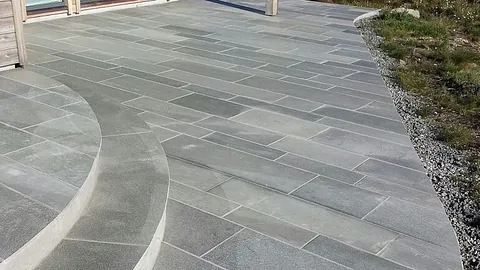 Grå steinheller lagt i mønster på uteplass med avrundede trappetrinn.